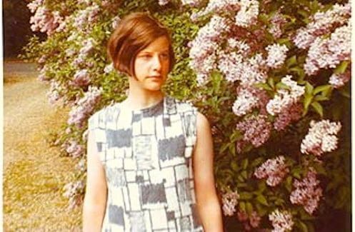 Image of Veronica Forrest-Thomson in front of a wall of flowers.