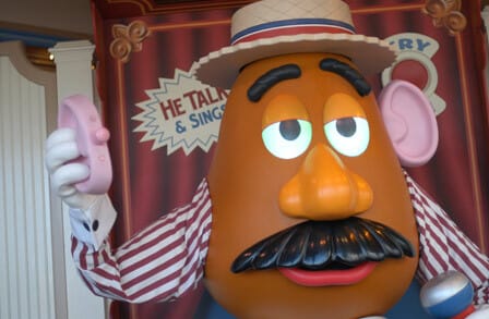 Mr. Potato Head toy wearing a striped shirt and hat with an ear in his hand