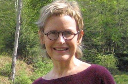 Poet Kate Farrell outdoors in front of trees.