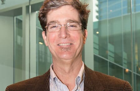 Headshot of writer Kenn Nesbitt in a tweed blazer in front of a glass building.