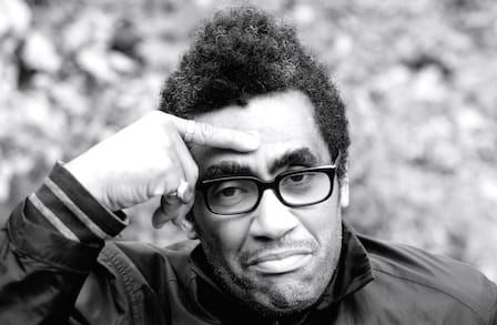 Black and white headshot of poet Thomas Sayers Ellis, with a finger to his brow.