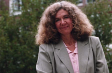 Poet Cleopatra Mathis standing in front of shrubbery.