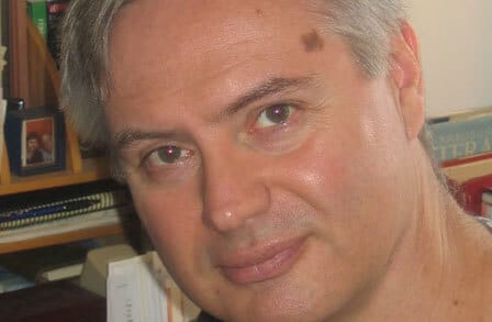 Headshot of poet Ned Balbo in front of a bookshelf.