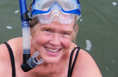 Color photograph of poet Freya Manfred wearing a scuba mask emerging from a body of water