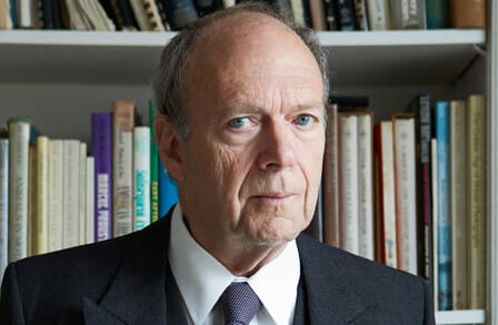 Headshot of writer Frederick Seidel in a suit in front of a bookshelf.