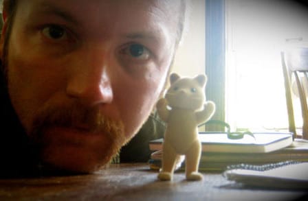 Poet Matthew Rohrer rests his head on his desk, next to a small  upright animal figurine.