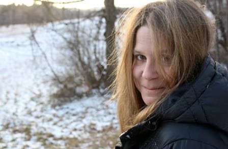 Poet Katie Peterson wearing a coat in the snow, turning back to face the camera.