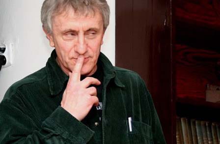 Cropped photo of poet Piotr Sommer raising a finger to his lips.