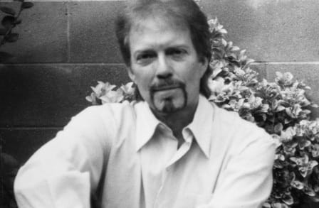 Black and white headshot of poet Charles Harper Webb in front of flowers.