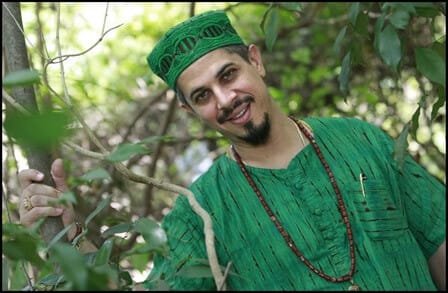 Titled headshot of poet Adrian Castro in a green shirt and hat.