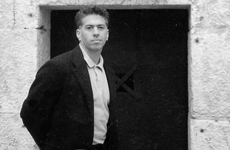 Black and white headshot of writer David Gewanter in a suit in a doorframe.