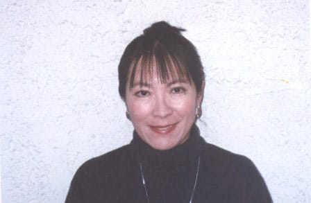 Headshot of poet Amy Uyematsu in front of a white wall.