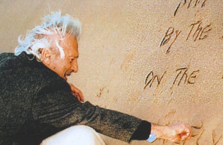 Image of Samuel Menashe writing in the sand