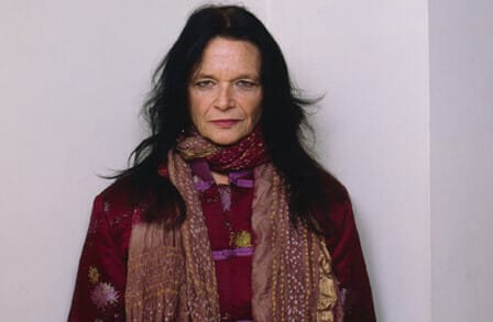 Headshot of poet Anne Waldman in front of a white wall.