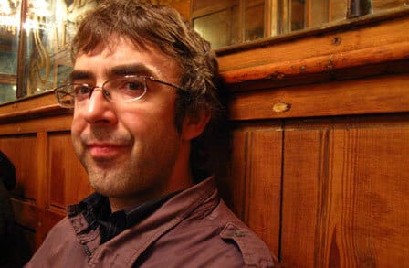 Headshot of poet David Wheatley sitting at a wooden booth.