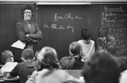 Image a Kenneth Koch smiling in front of a classroom.
