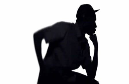Silhouette of a person sitting, arms akimbo, and wearing a baseball hat