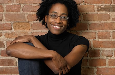 Image of Jacqueline Woodson posing in front of a brick wall.