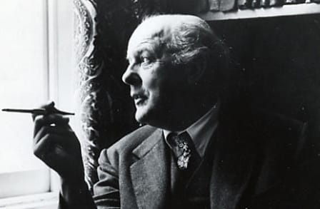 Headshot of poet John Betjeman, holding a fountain pen and looking out a window.