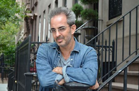 Poet Ben Downing standing in front of stoops with his arms crossed.