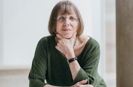 Portrait of Carina Romano in a green sweater, leaning forward  in a pensive position with her left hand under her chin.