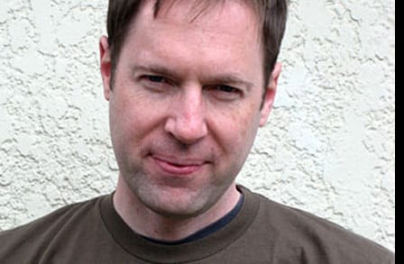 Poet Dobby Gibson in front of a white wall.