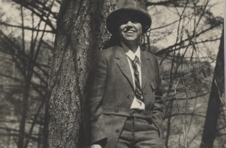 Poet Florence Ripley Mastin in a suit and hat, leaning against a tree.