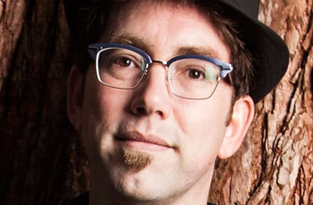 Headshot of poet Mike Chasar leaning against a tree.