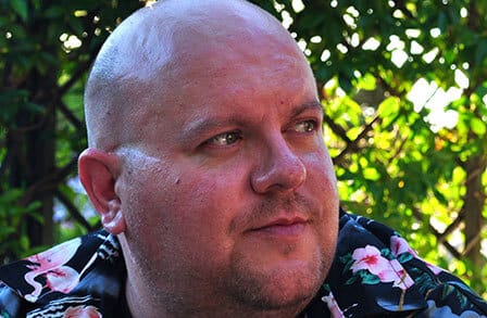 Headshot of poet Alan Gillis  in front of a trellis.