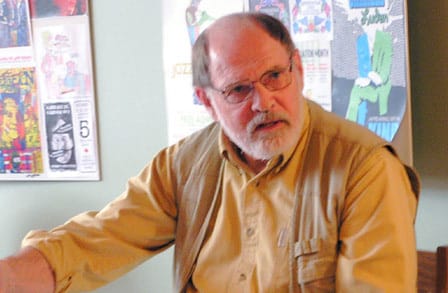 Poet David ALlen Evans in a yellow button down shirt, extending his arm.
