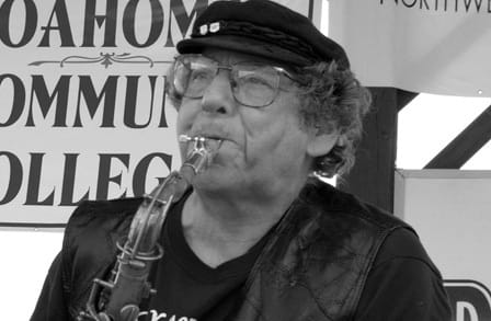 Black and white headshot of poet Dick Lourie, playing saxophone.
