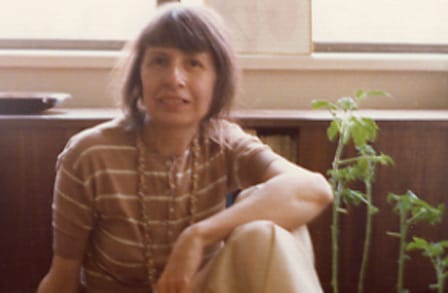 Poet Amy Clampitt sitting by plants.