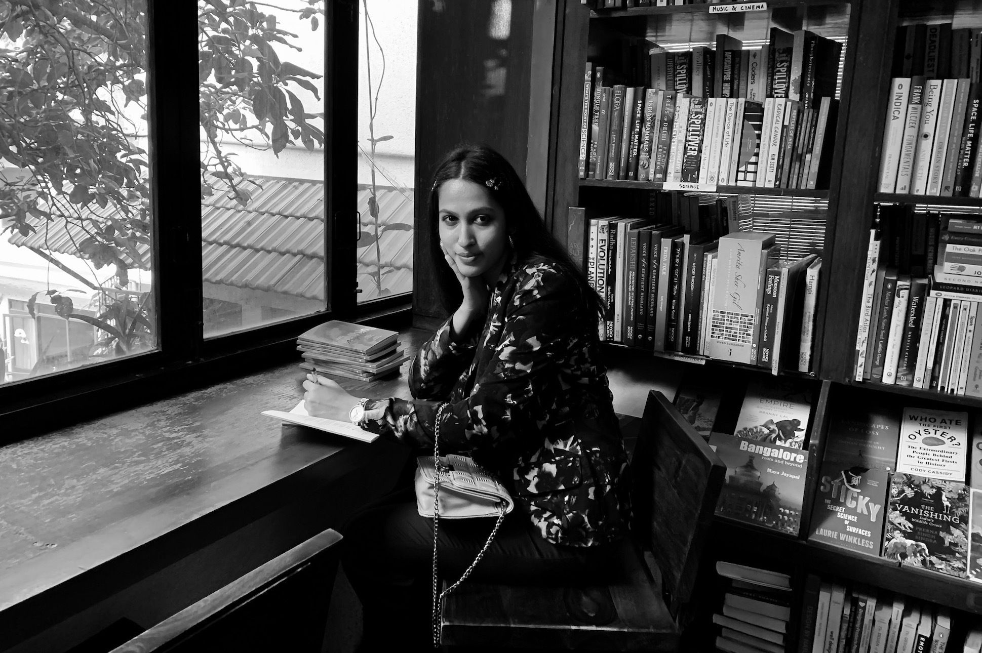 A woman with long hair sitting by the window and bookshelf