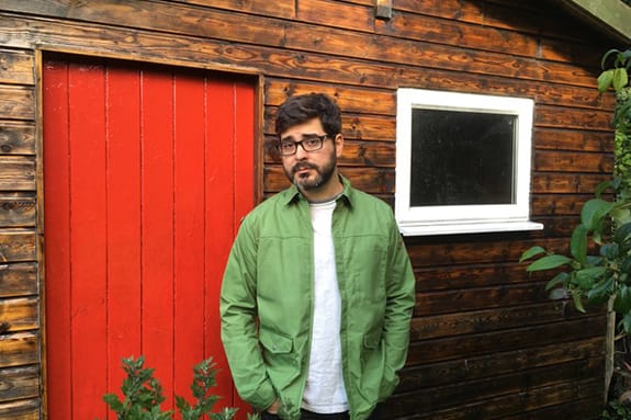 Evan Jones stands in front of a cabin or cottage with a red door.