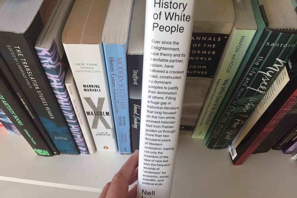 "The History of White People" being picked from a shelf of books