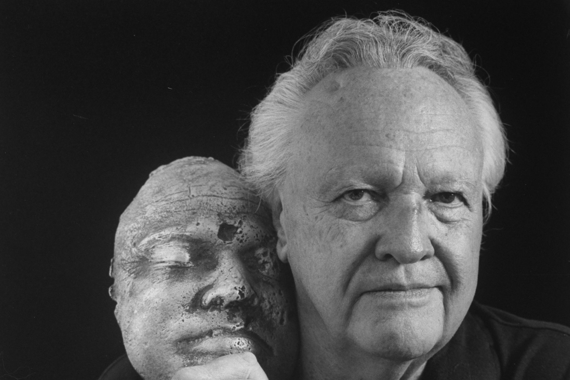 Author James Dickey holding cheek-to-cheek with a ceramic mask of his face designed by Billy Dunlap, at home.