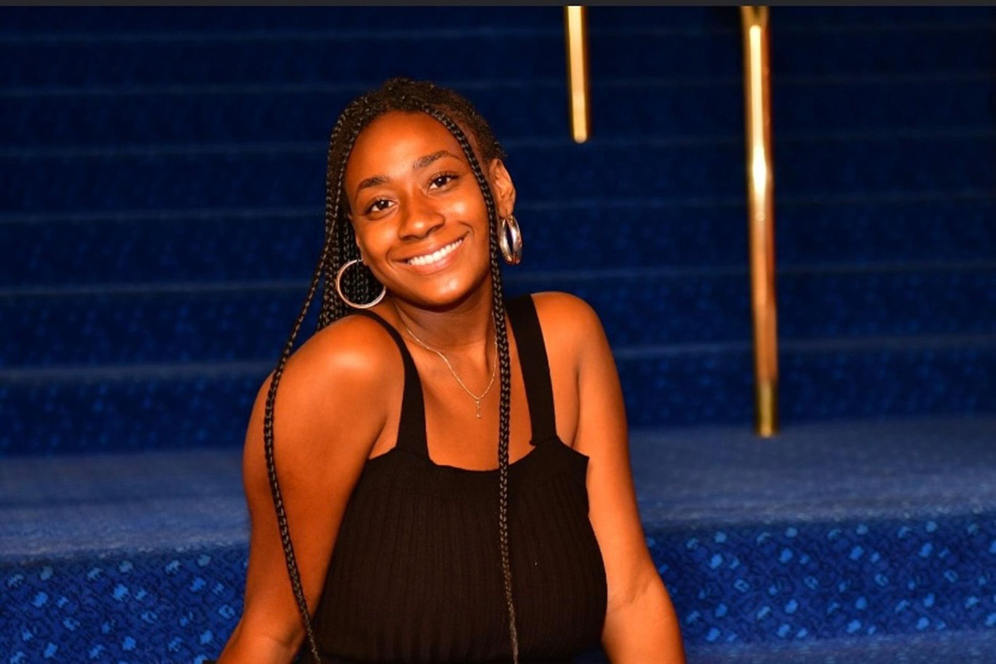 A black woman in a black top sitting on staircase with blue velvet carpet