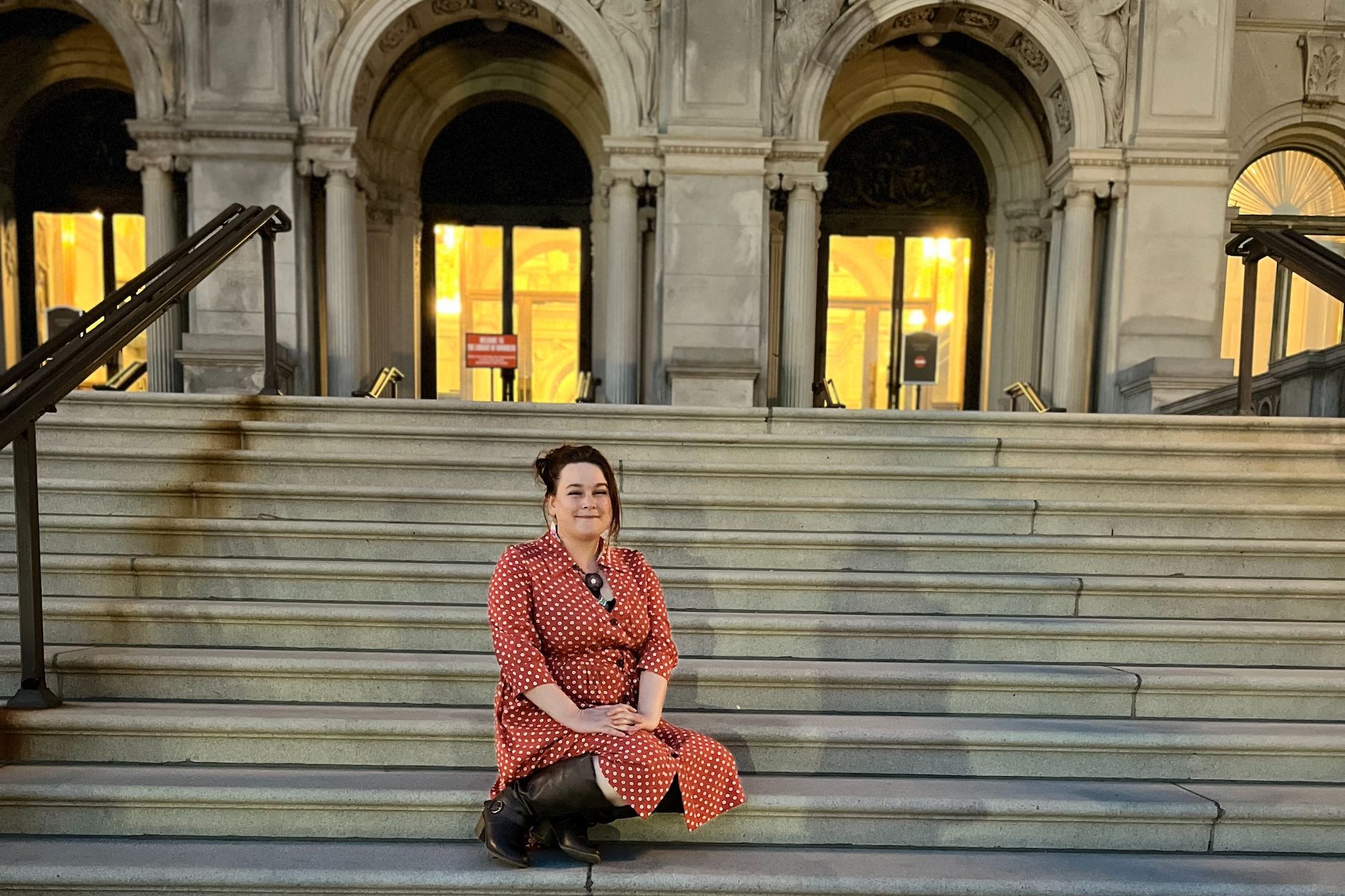A woman with a red plaid dress sitting on the stairs outside of a historical building