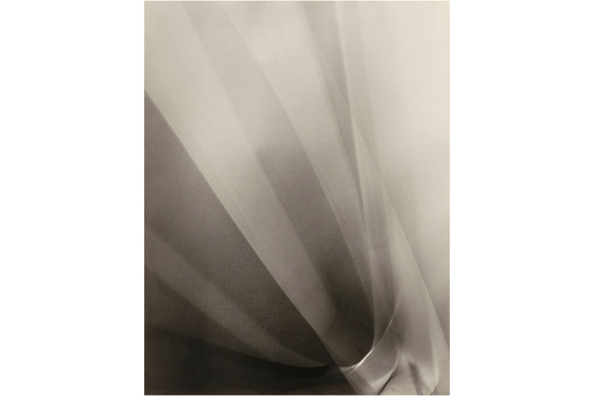Black and white photograph of white fabric or paper with vertical folds, like a fan, on an angle.