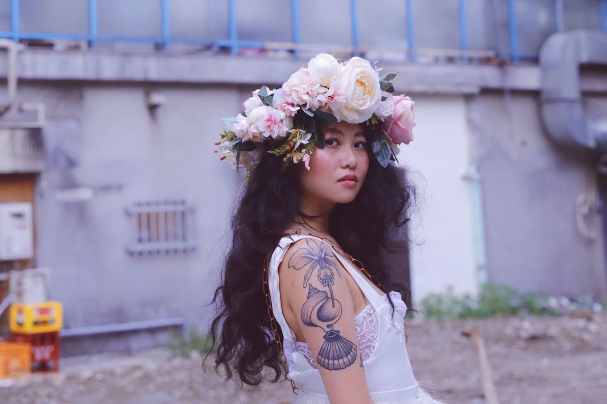 Poet Shan Xiao Yue wearing a white dress, with a flower crown on her head, and tattoo on her right arm.