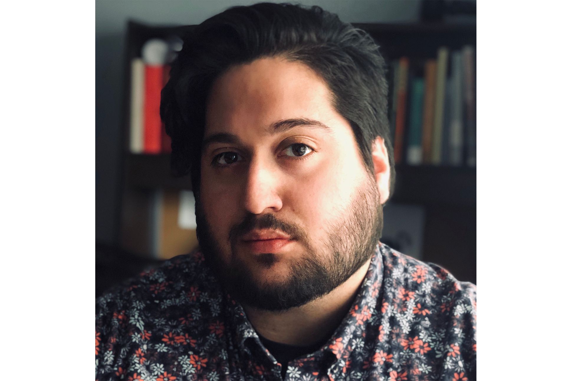 Man in floral shirt in front of a bookshelf