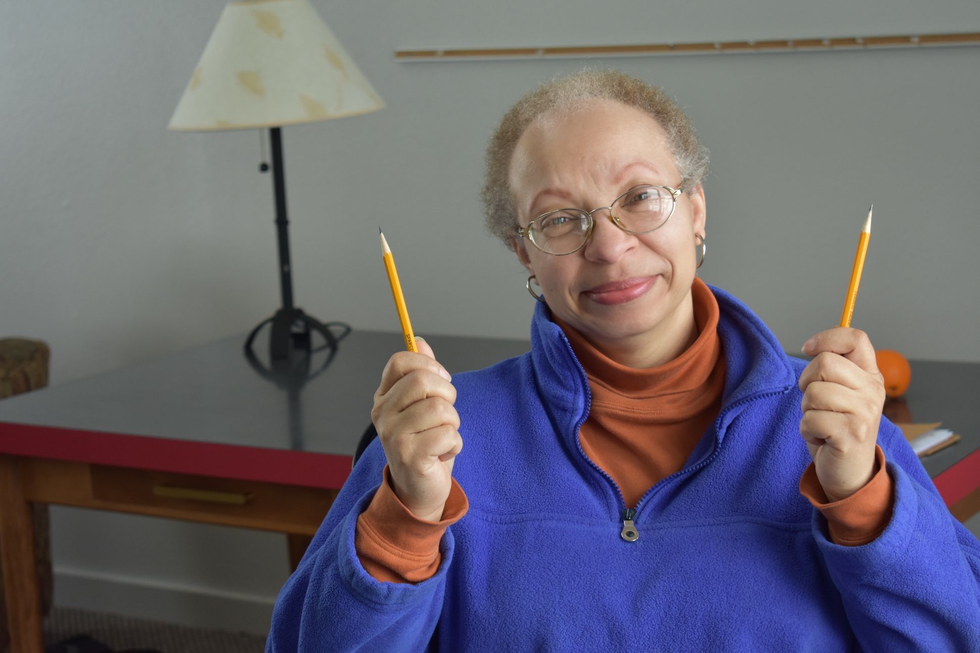 A woman in a purple sweater holding up two pencils on her hands