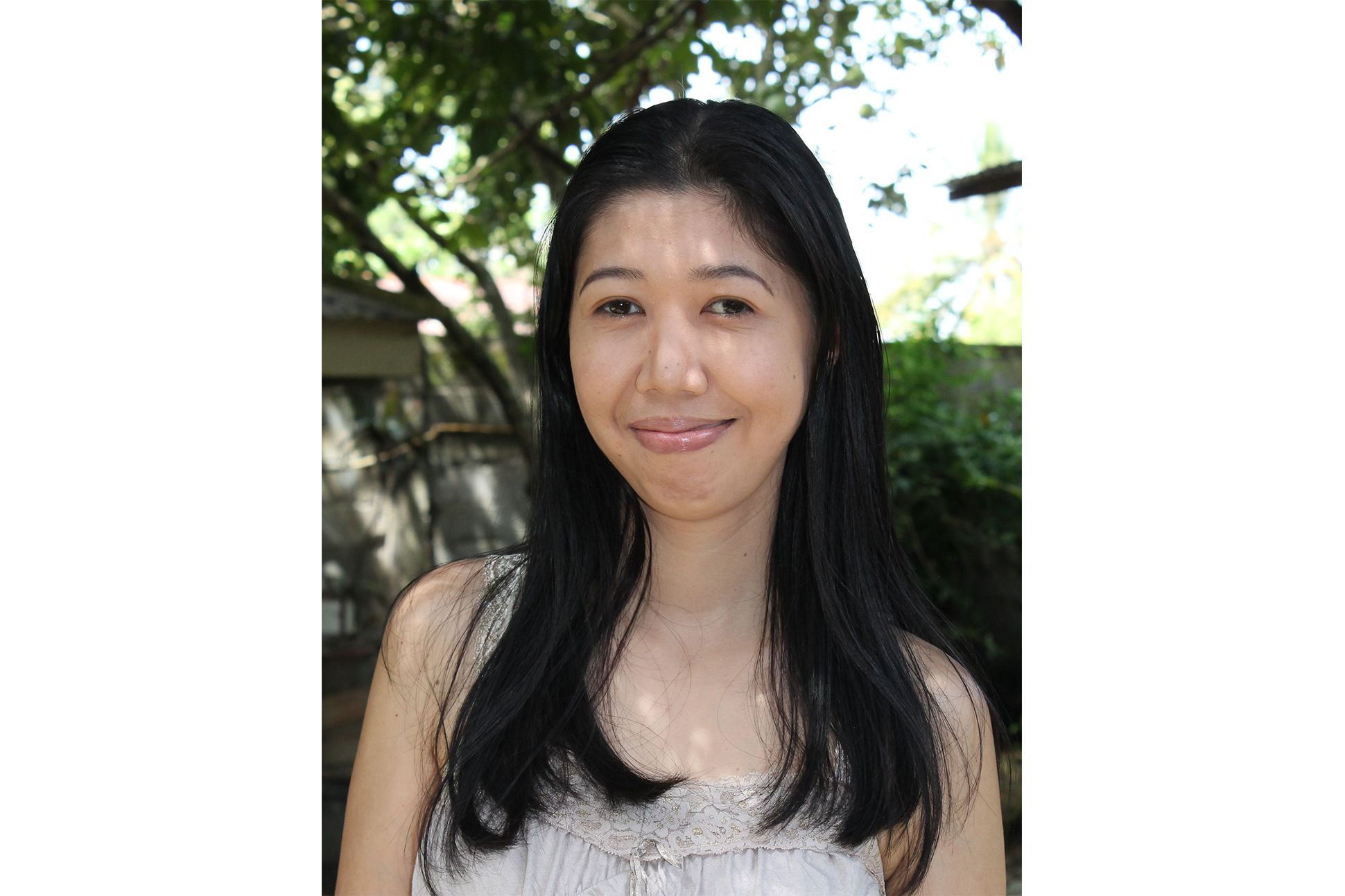 Photo of an Asian woman smiling  in front of trees