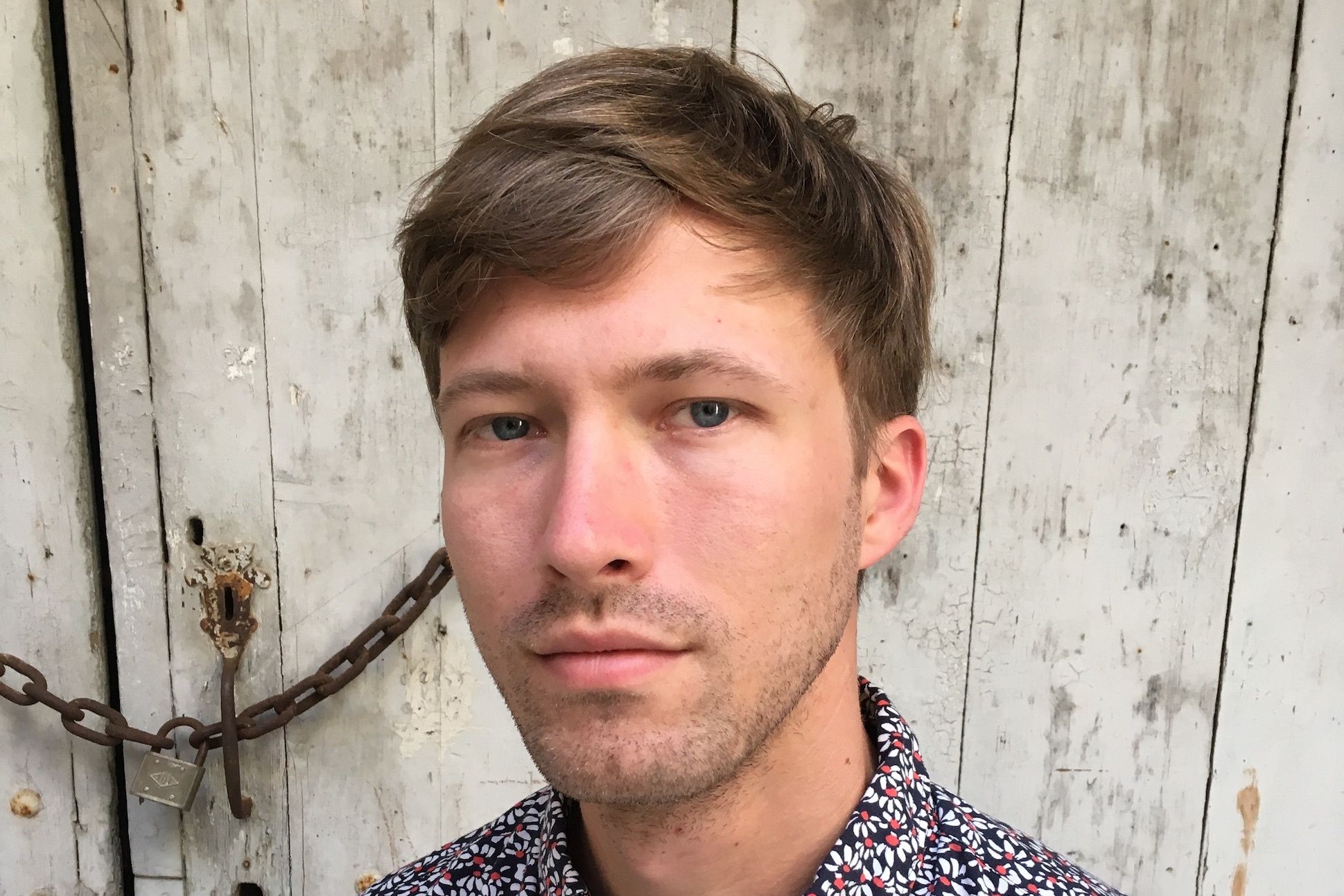 White man in floral shirt in front of fence