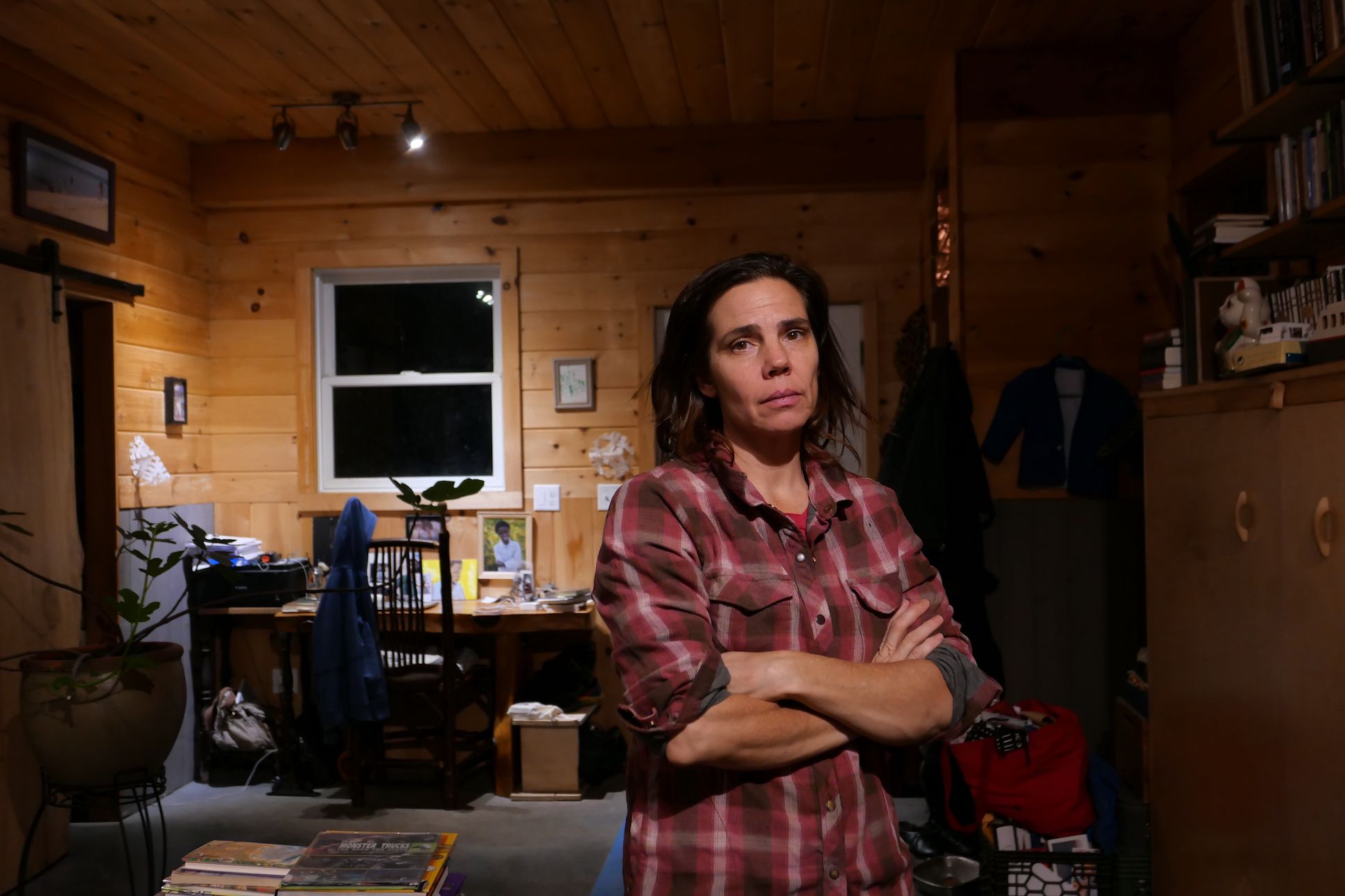 A woman with dark red plaid shirt standing inside a study with wooden walls