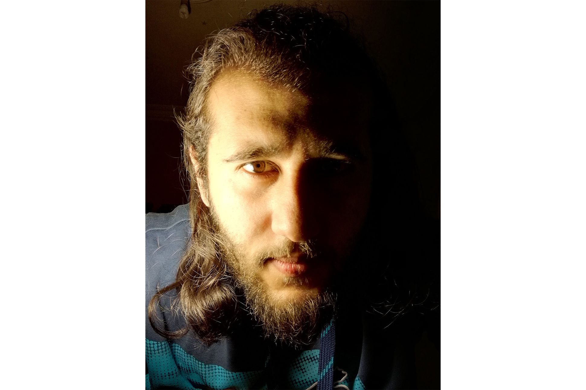 A close up shot of a man with long hair and beard and half of his face in the light and the other half in the dark