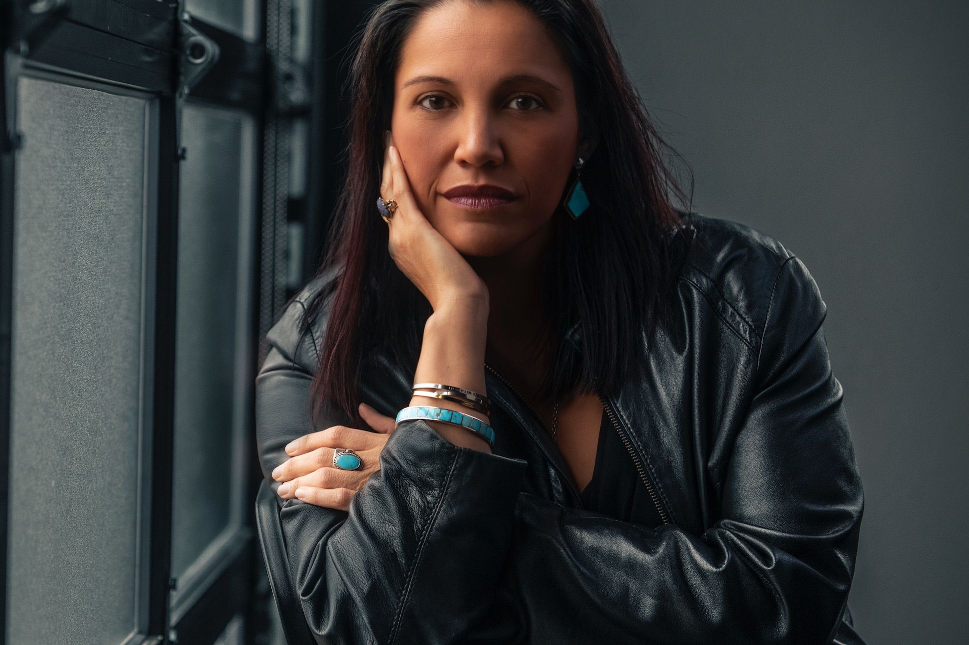 A woman in a black jacket posing by glass windows