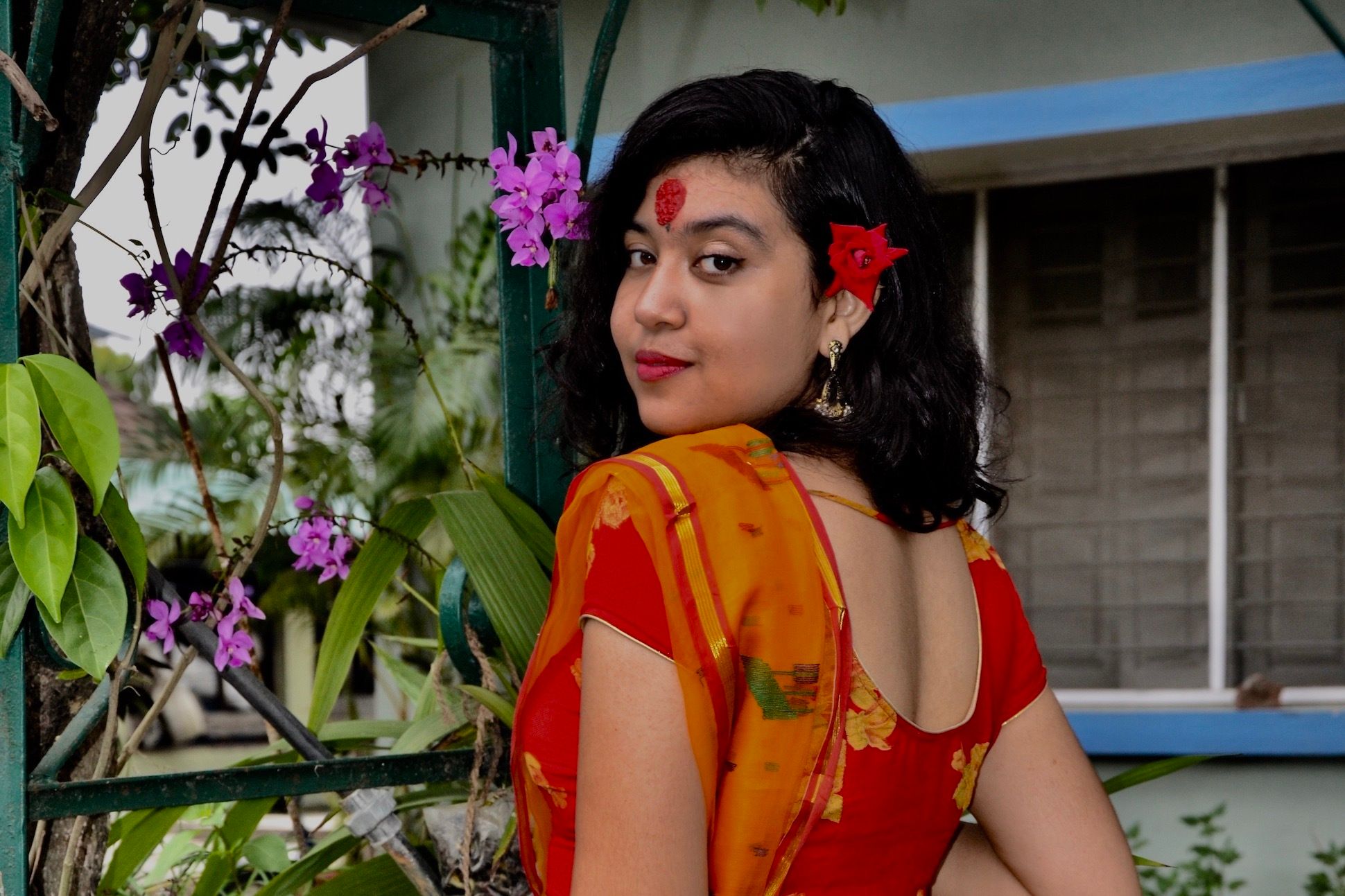 Woman in red and orange traditional Indian clothing standing in front of plants