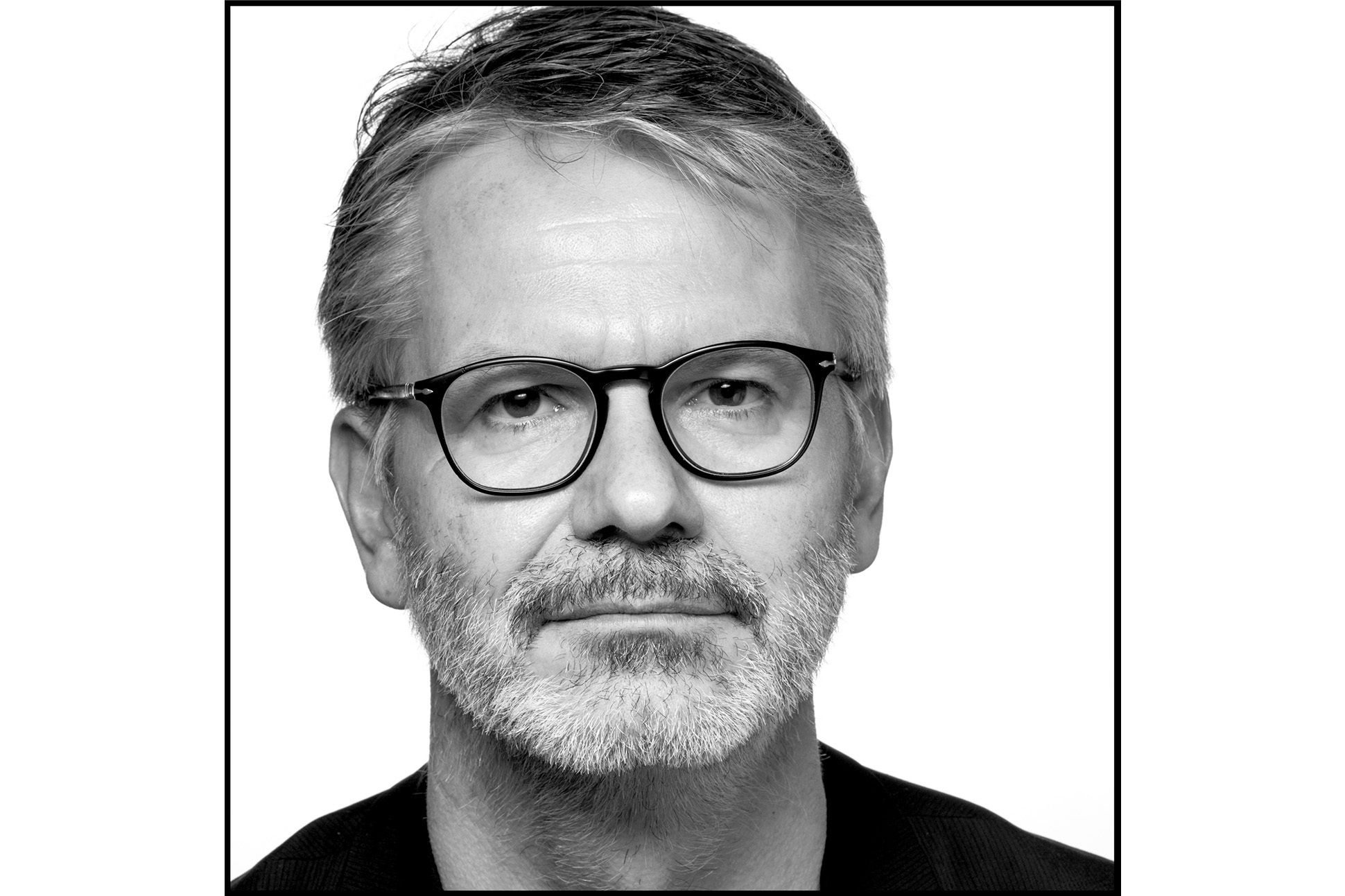 Black and white portrait of a man with glasses and beard wearing a black t-shirt