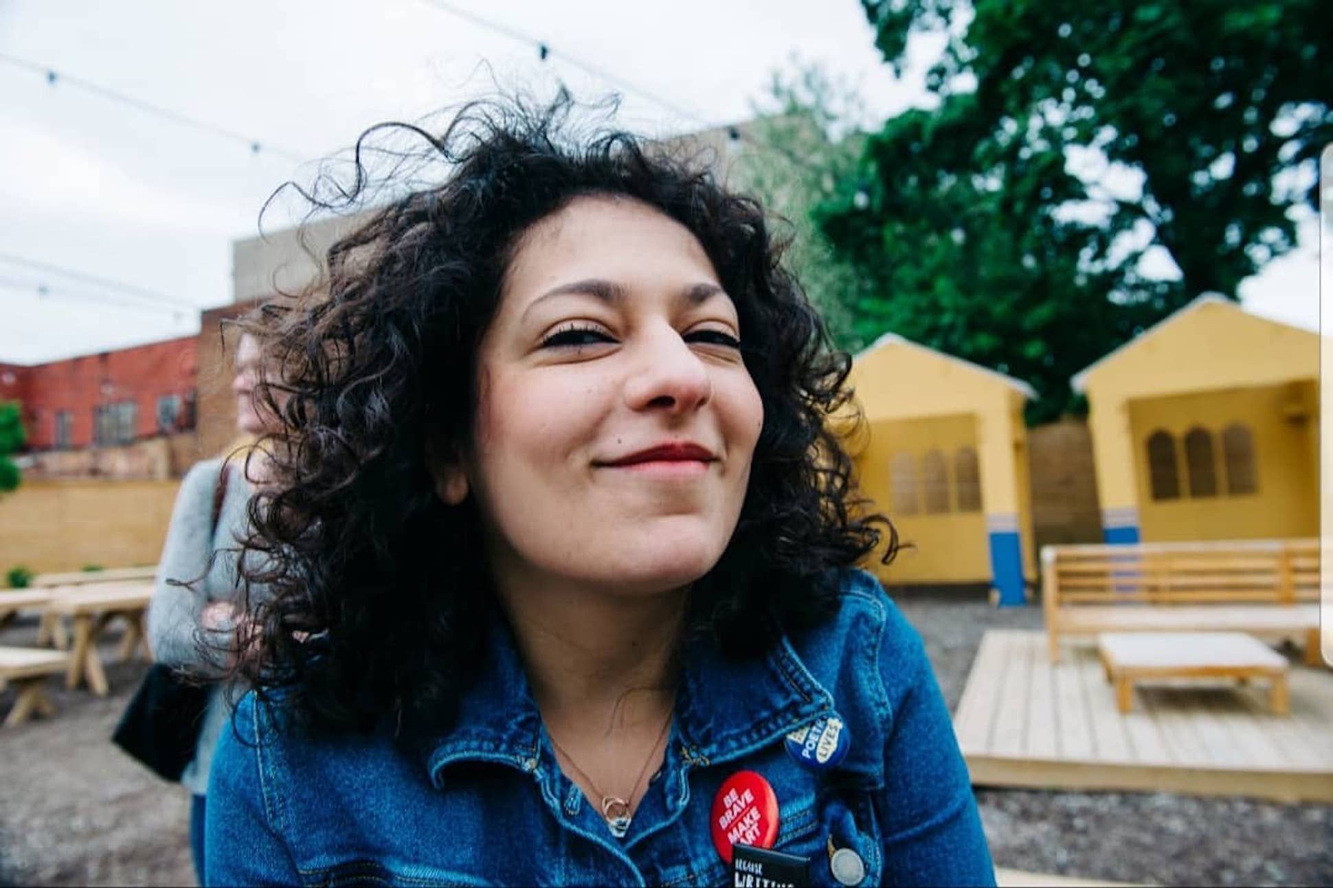 Woman with curly hair in a denim jacket in what appears to be a children playground